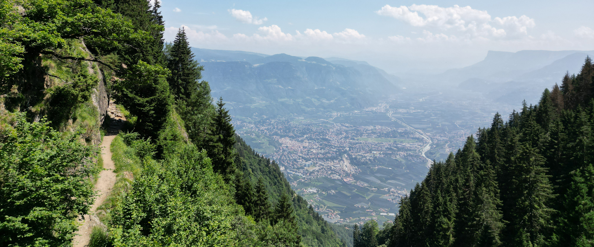 Meran high alpine route near Algund Narrow hiking trail on a wooded mountainside, wide view of the valley below